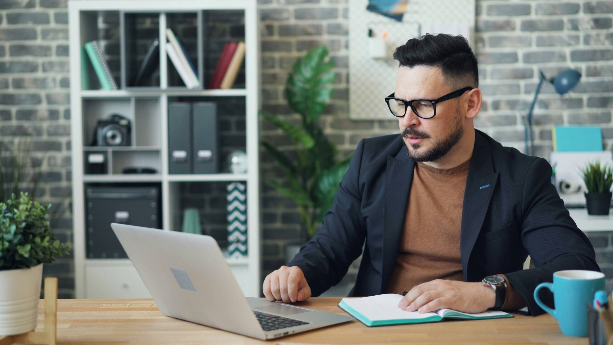Young professional man working on a laptop in a modern office with notebook in hand