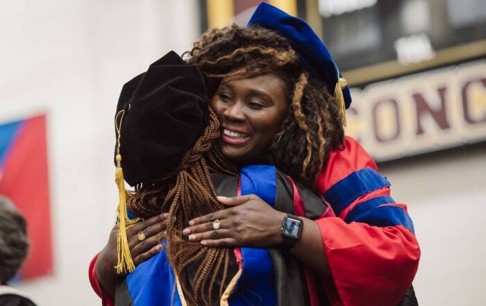 Two graduates in academic regalia embracing at a graduation ceremony, celebrating educational achievement and career growth.