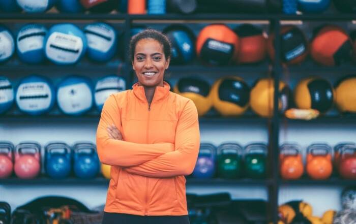 Smiling female sports nutrition expert standing confidently in front of kettlebells, symbolizing success in fitness and career development