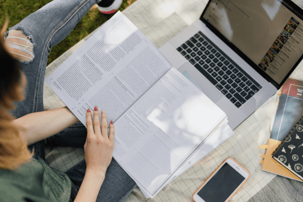 Student studying exercise science materials with laptop and notes outdoors